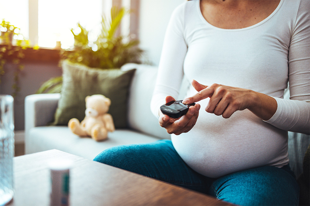 Pregnant female sitting on couch with glucometer.